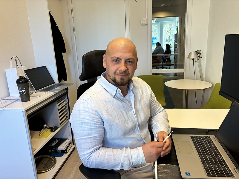 Porträtt av ung kvinna med långt hår och svarta kläder. I bakgrunden stora fönster. 